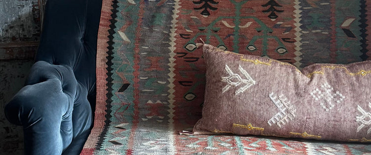 Blue velvet sofa draped with a vintage kilim and an embroidered cushion