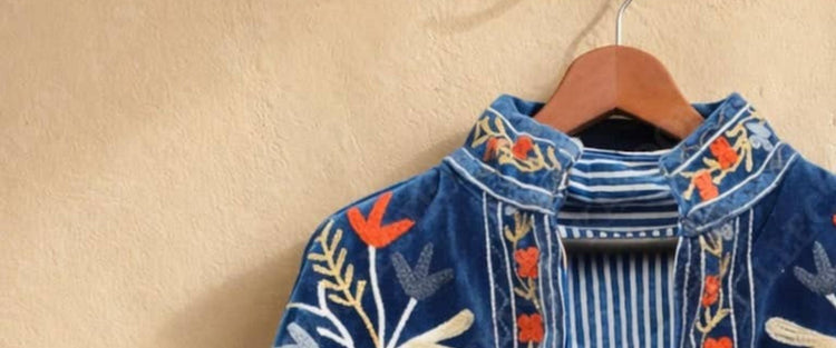 Hand-embroidered blue velvet jacket on a wooden hanger against a plaster wall